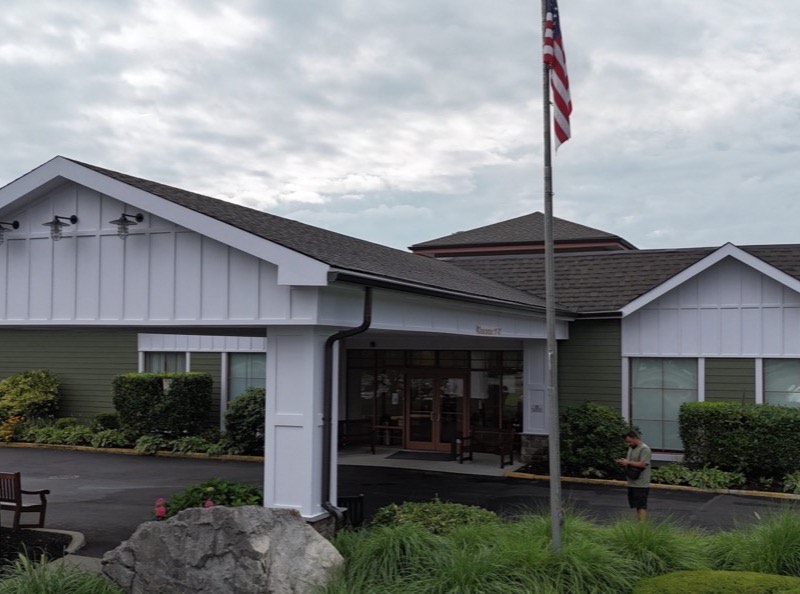 After: the same building refinished with green board-and-batten siding, white gable ends, stone-base entry columns and a new architectural shingle roof