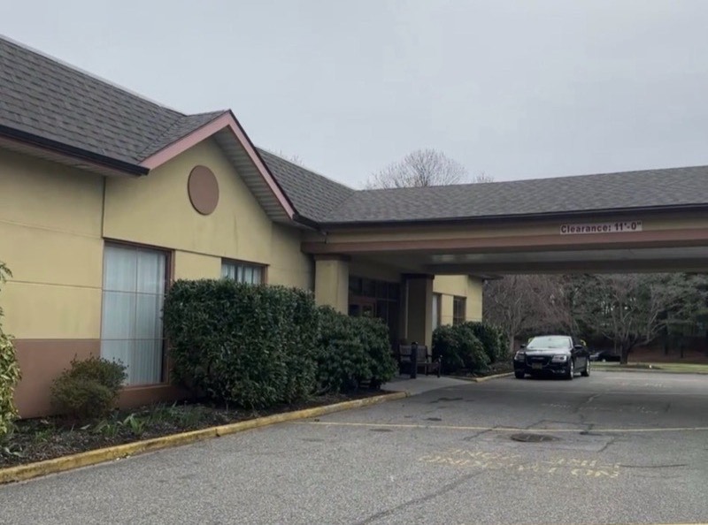 Before: dated building exterior with tan stucco, pink trim and a worn dark shingle roof over the entry canopy